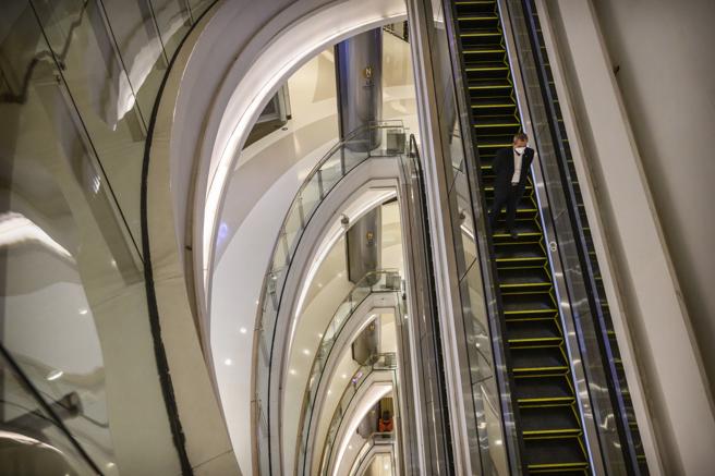 Un hombre con mascarilla desciende por una escalera mecánica en un edificio del distrito central de negocios de Pehín