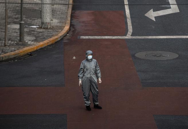 Un hombre con traje protector espera para cruzar una calle en Pekín