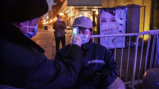 Un trabajador chino con una mascarilla registra la temperatura de un colega en Pekín, 12 de febrero, 2020